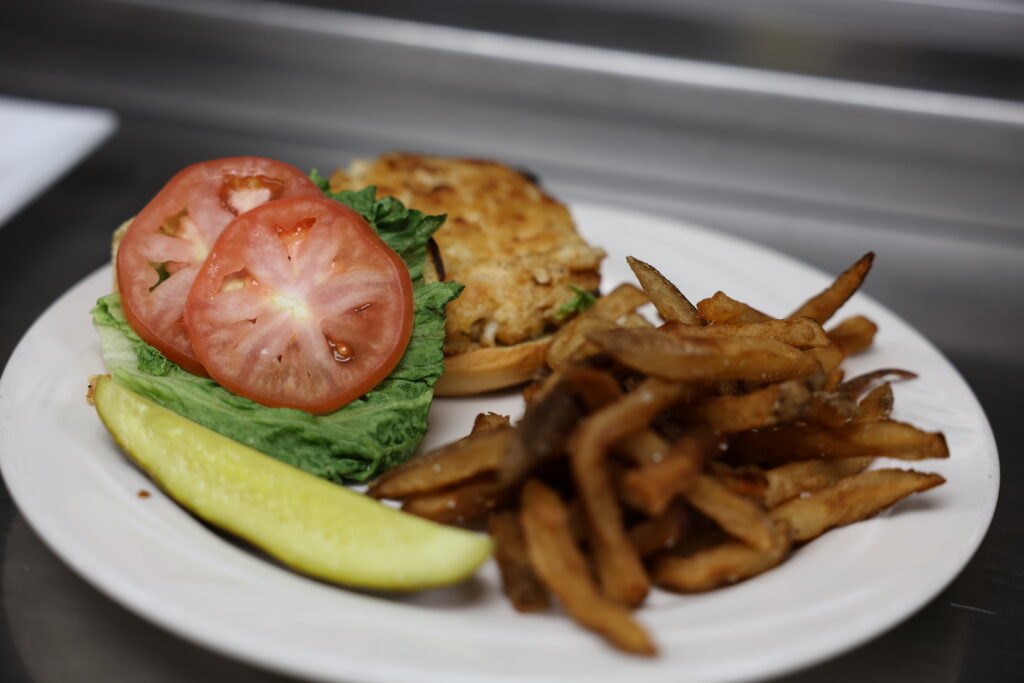 A plate with a chicken sandwich topped with lettuce and tomato, a serving of French fries, and a pickle spear on the side.